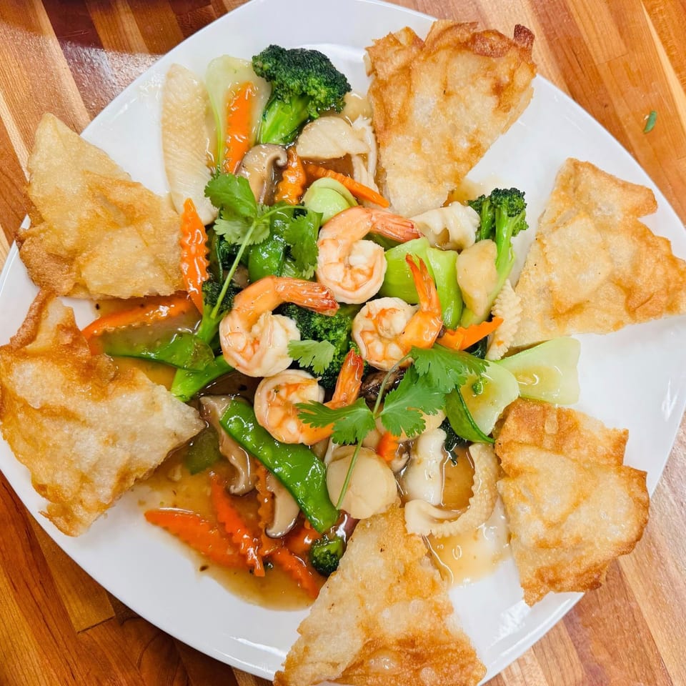 Vietnamese stir-fry with shrimp, vegetables, and crispy wontons on a white plate.
