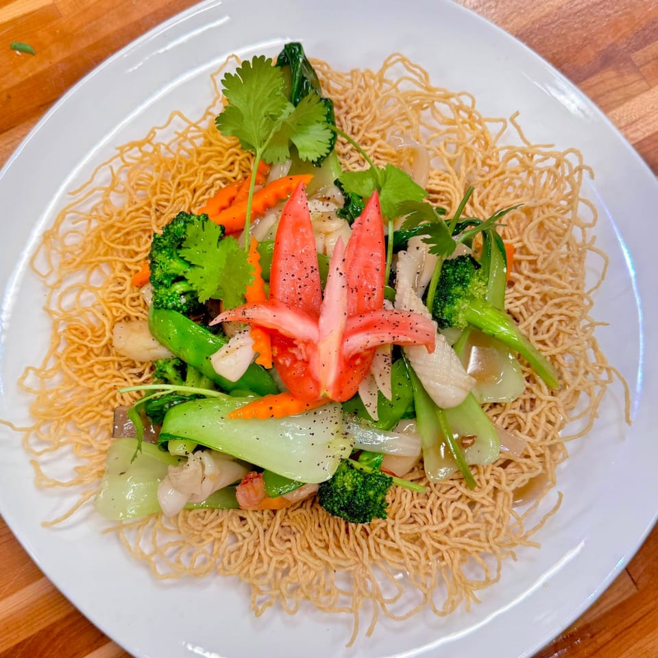 Vietnamese crispy egg noodles with stir-fried vegetables, seafood, and a carved tomato garnish.