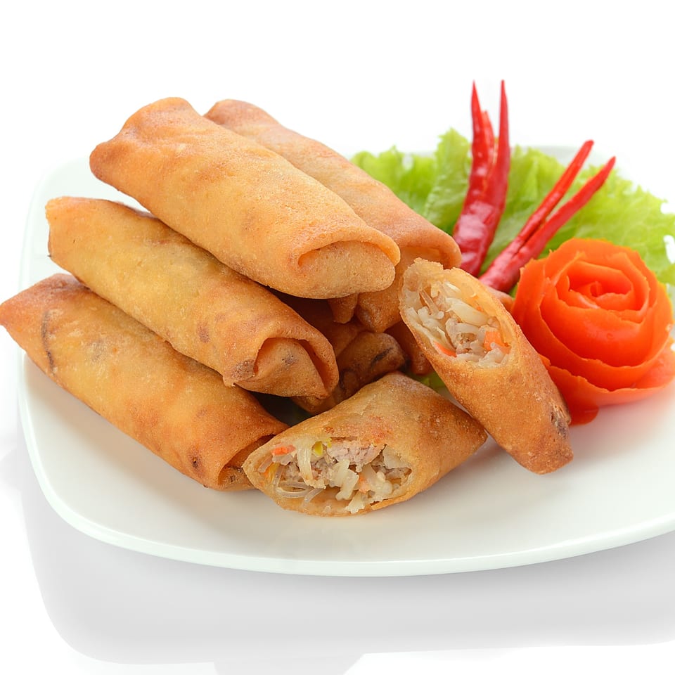 Crispy Vietnamese spring rolls, one cut open to show filling, garnished with lettuce, chili, and tomato.