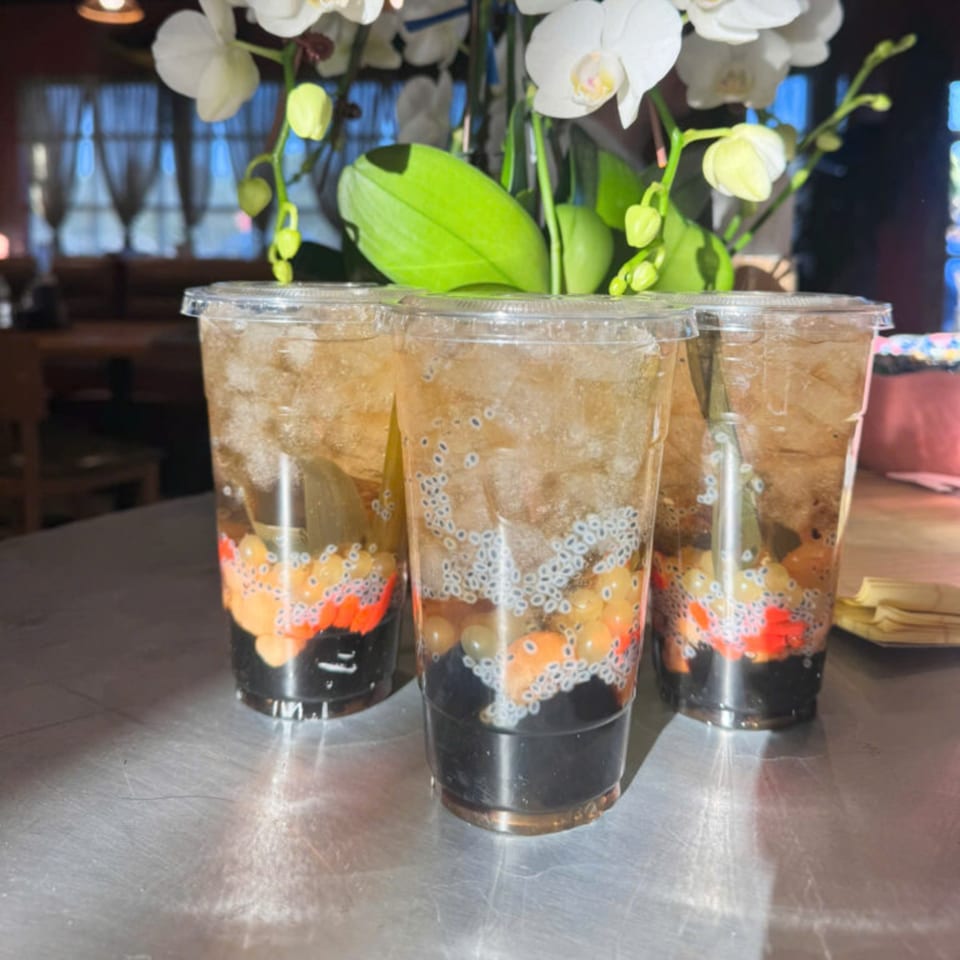 Three Vietnamese drinks with colorful jellies, basil seeds, and ice, on a metal table with orchids.