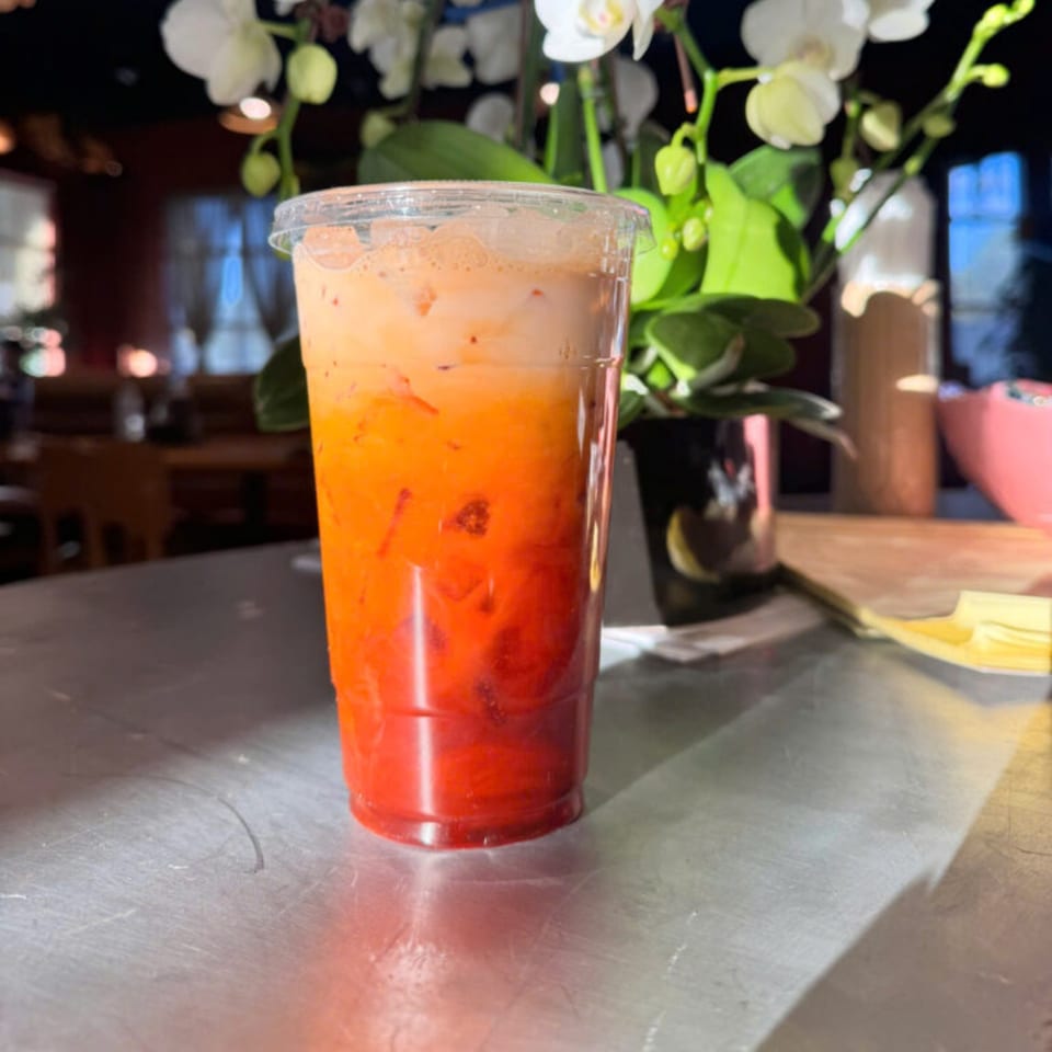A vibrant Vietnamese iced tea with distinct layers of orange and red, topped with cream.